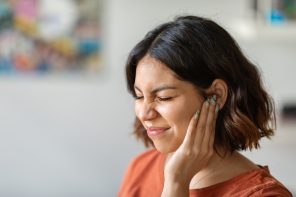 Sick young arab woman having ear pain at home, upset middle eastern female rubbing sore auricle with hand and frowning, suffering from otitis and acute ache, closeup shot with copy space